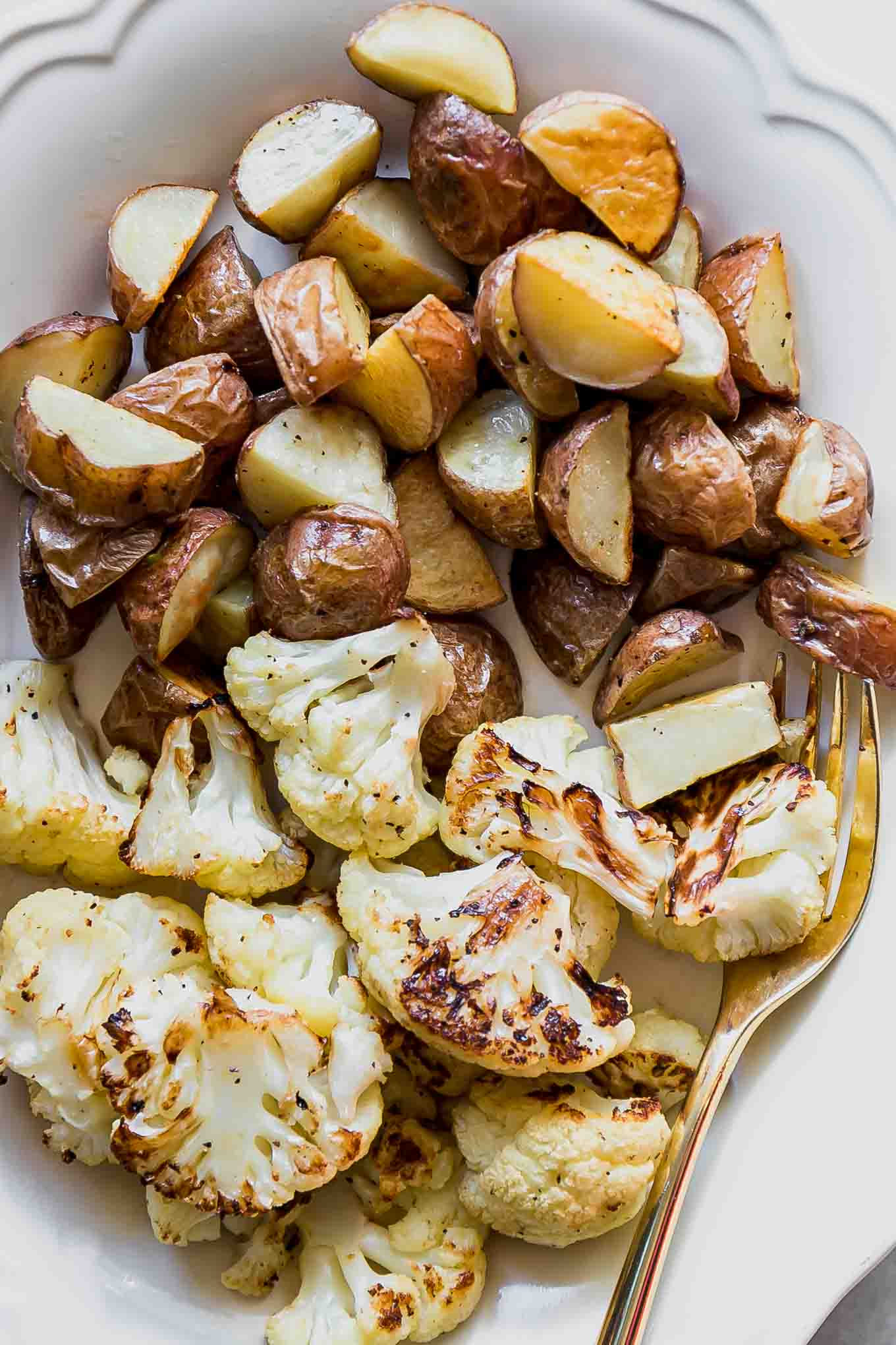 a close up of cauliflower and potatoes on a white side dish