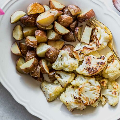 roasted cauliflower and potatoes on a white plate with a gold fork