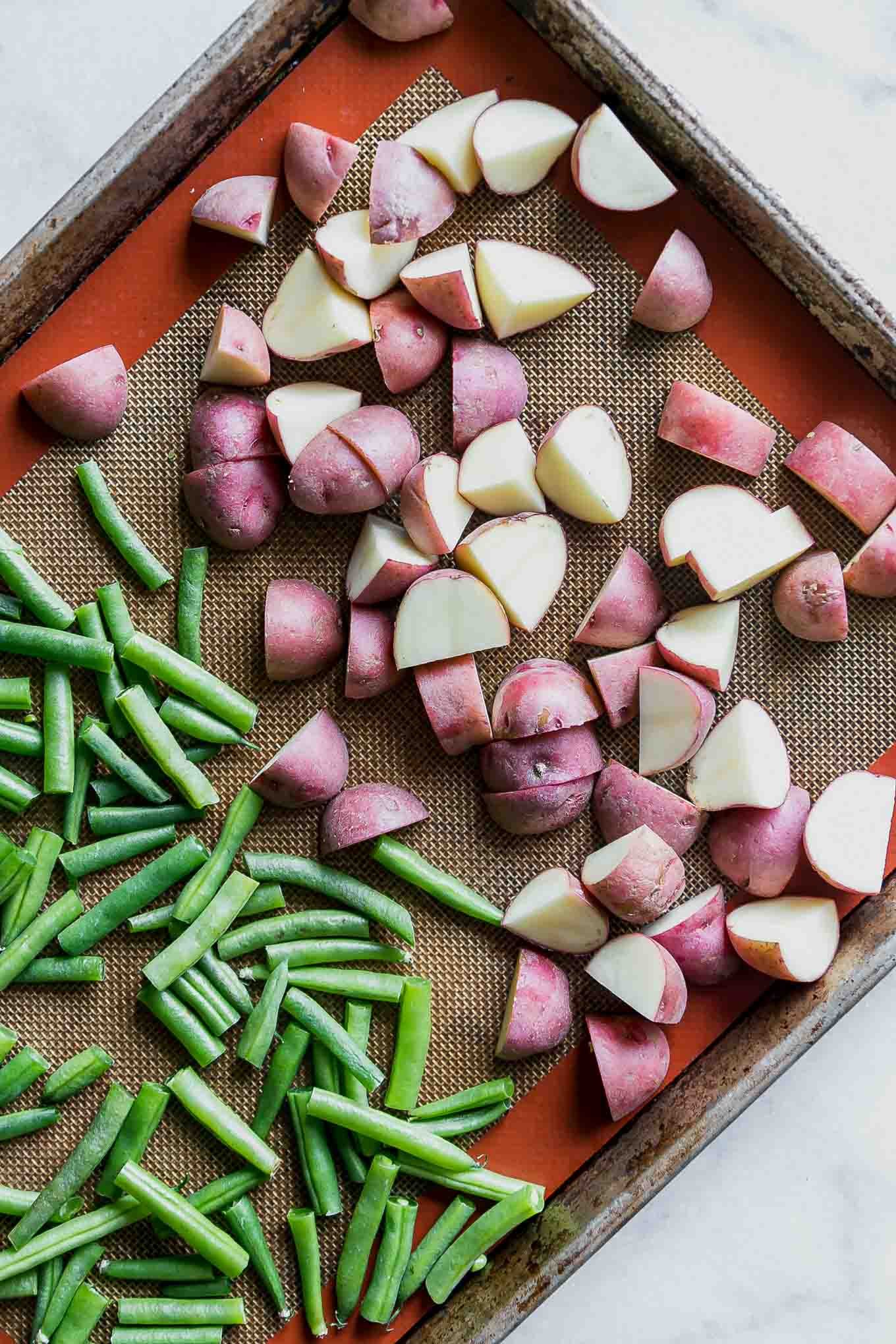 cut potatoes and green beans on a baking sheet before roasting
