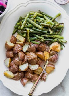 roasted potatoes and green beans on a white plate with a gold fork