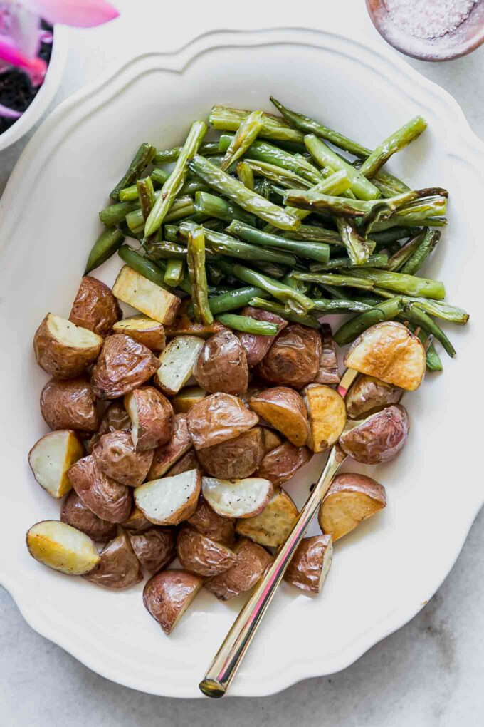 roasted potatoes and green beans on a white plate with a gold fork