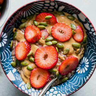 a blue bowl with oatmeal and fresh cut strawberries on a white table
