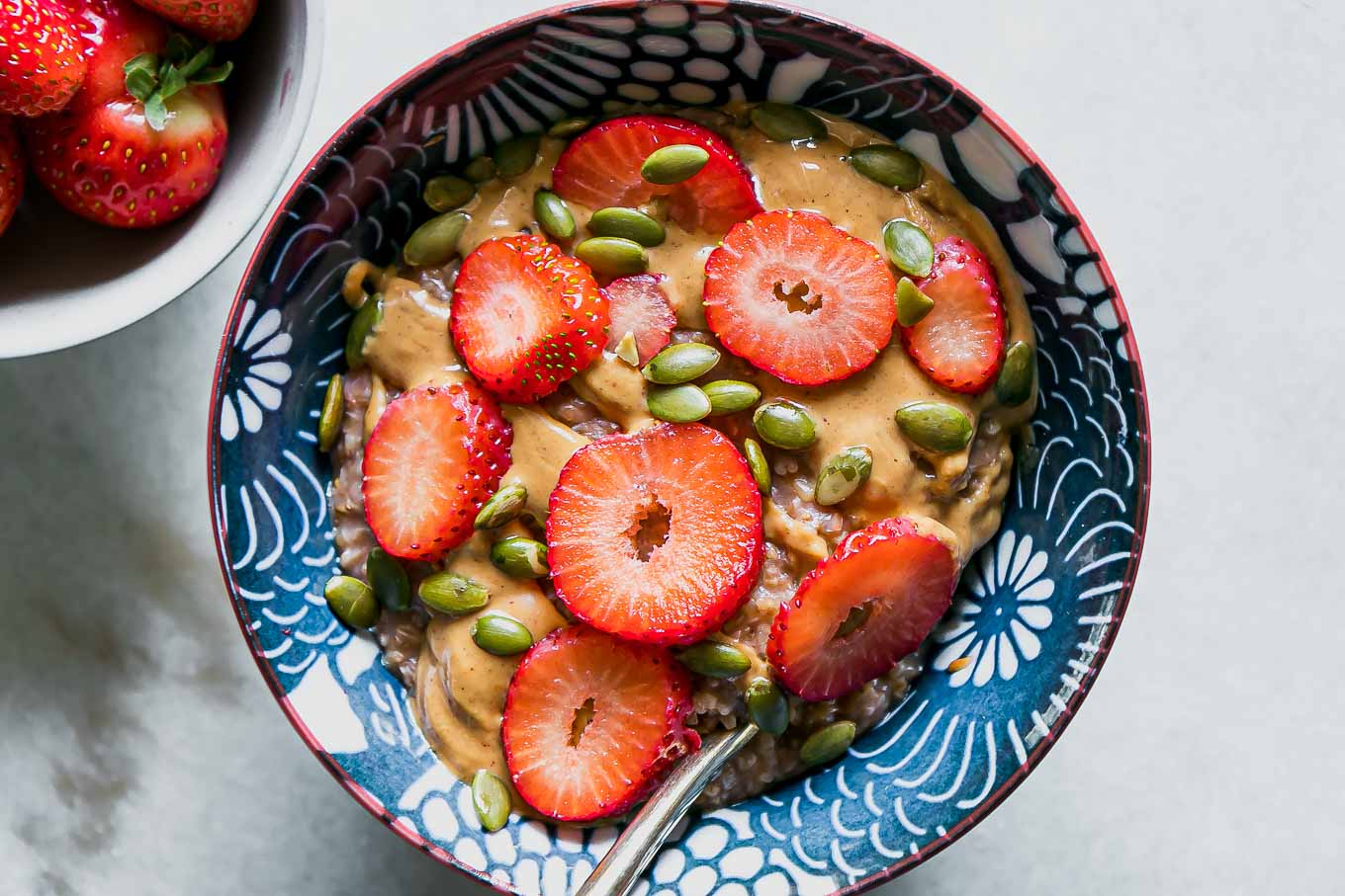 a blue bowl with oatmeal and fresh cut strawberries on a white table