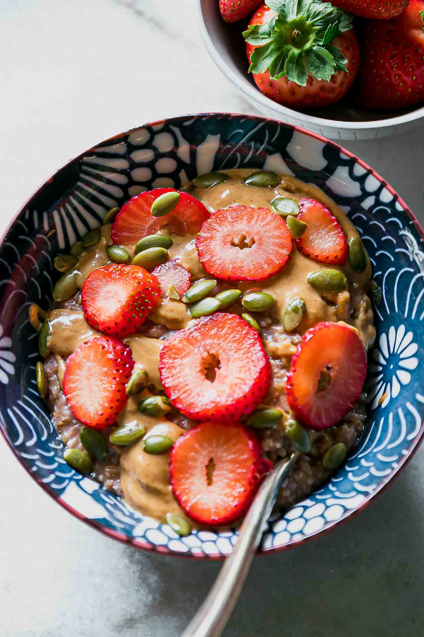 an oatmeal bowl with strawberries, nut butter, and seeds in a blue bowl