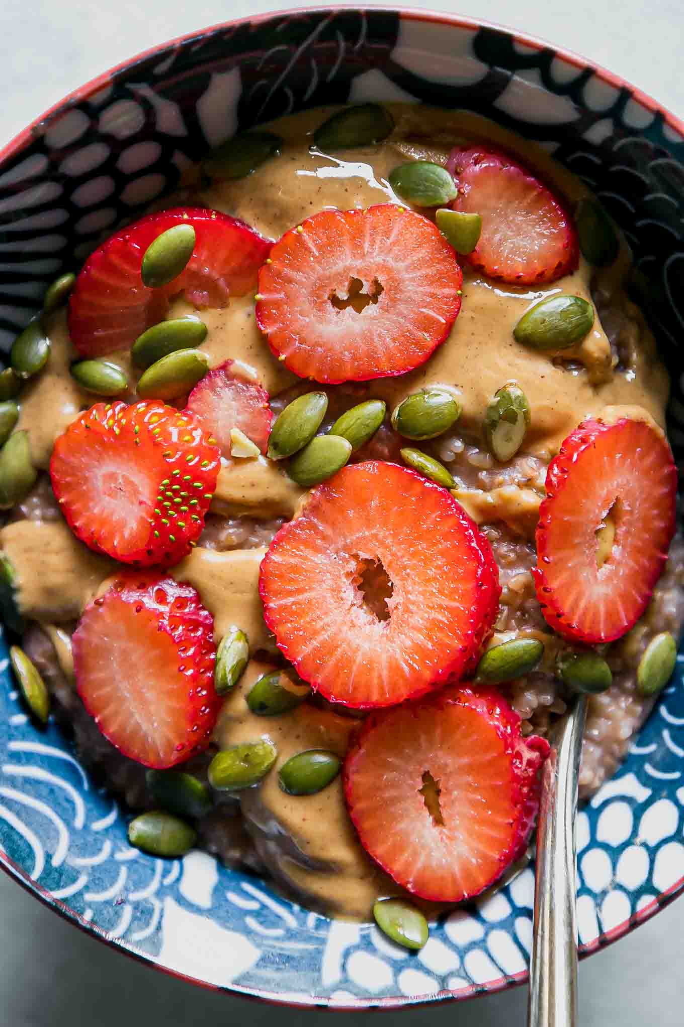 a close up photo of oatmeal with peanut butter, sliced strawberries, and pumpkin seeds