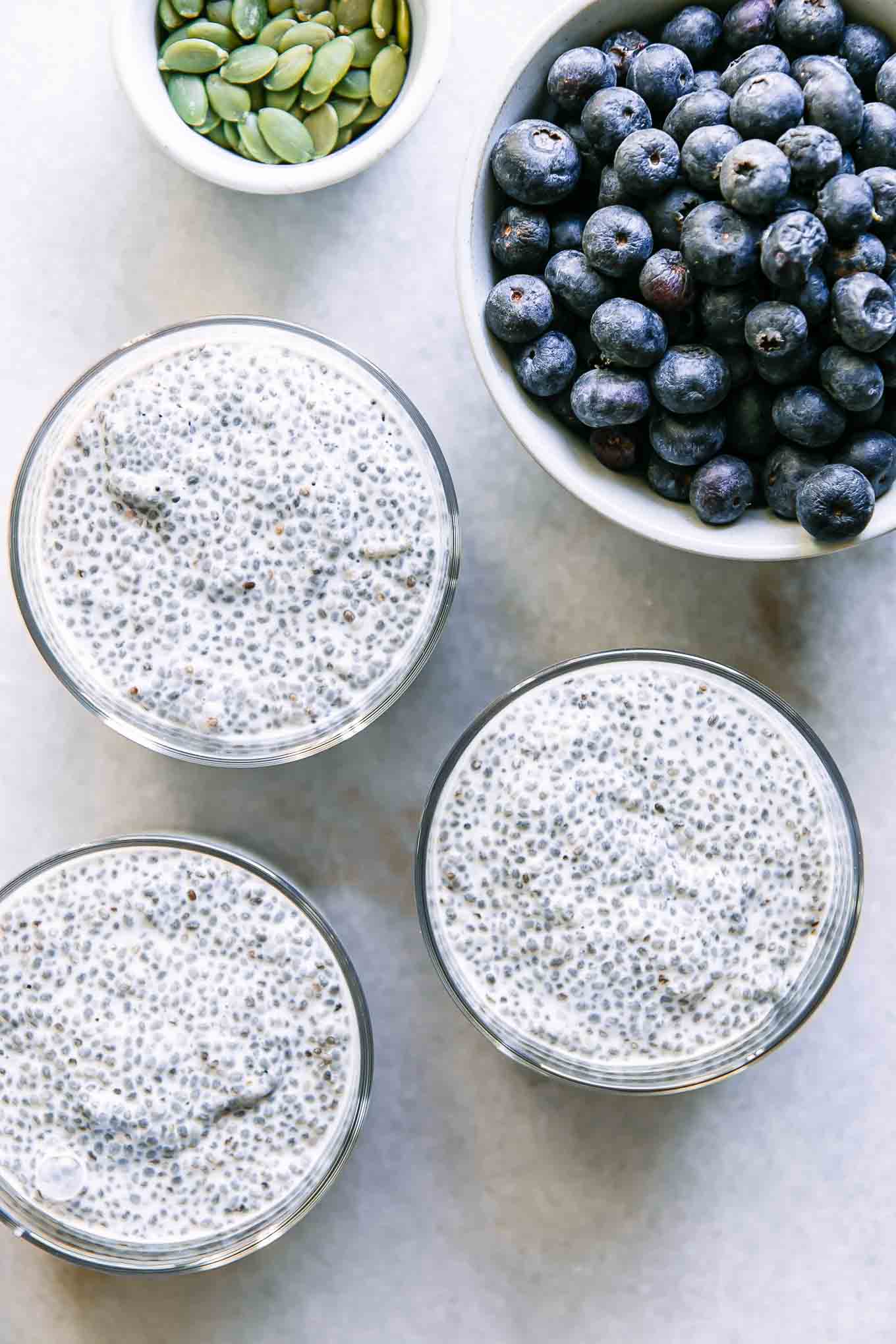 three bowls of chia seed pudding on a white table with a bowl of blueberries