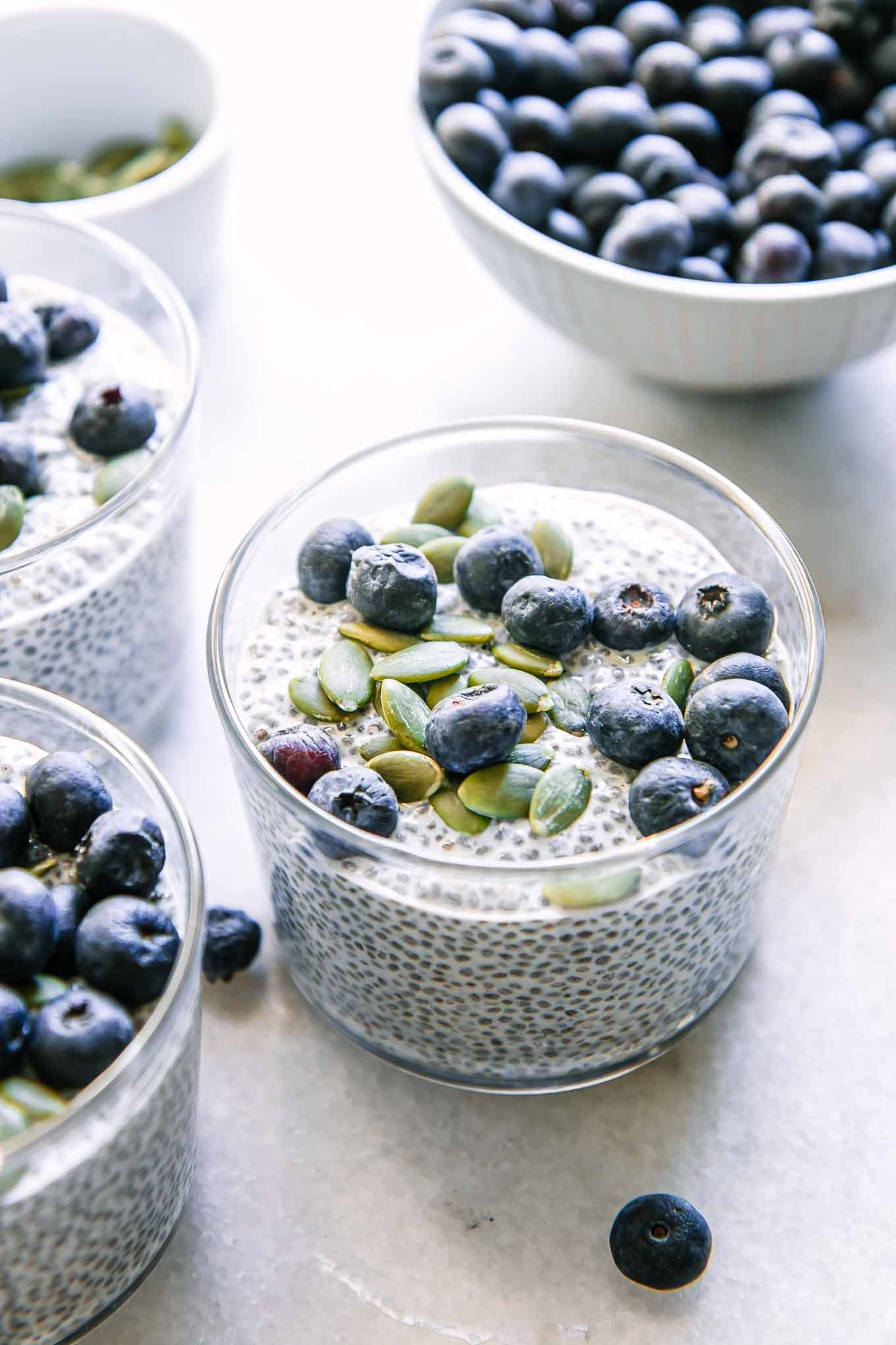 three glasses with chia seed pudding topped with blueberries on a white table