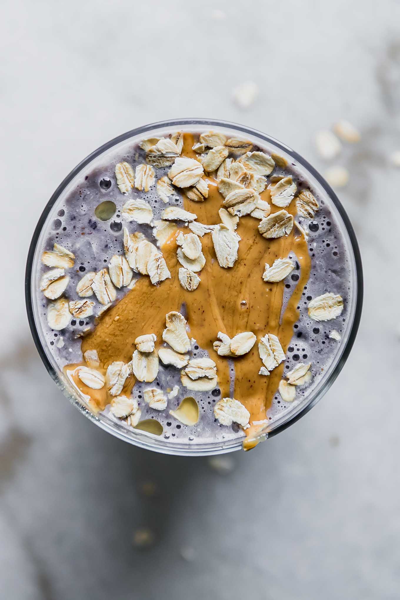 a close up photo of a blueberry smoothie with nut butter and garnished with oats