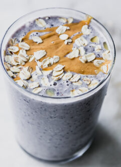 a blueberry and oatmeal smoothie in a glass with nut butter and rolled oats garnish