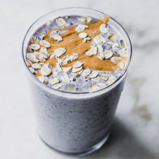 a blueberry and oatmeal smoothie in a glass with nut butter and rolled oats garnish