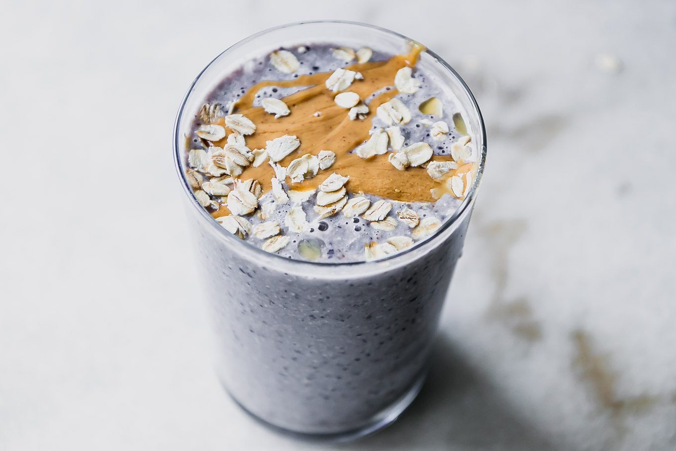 a blueberry and oatmeal smoothie in a glass with nut butter and rolled oats garnish