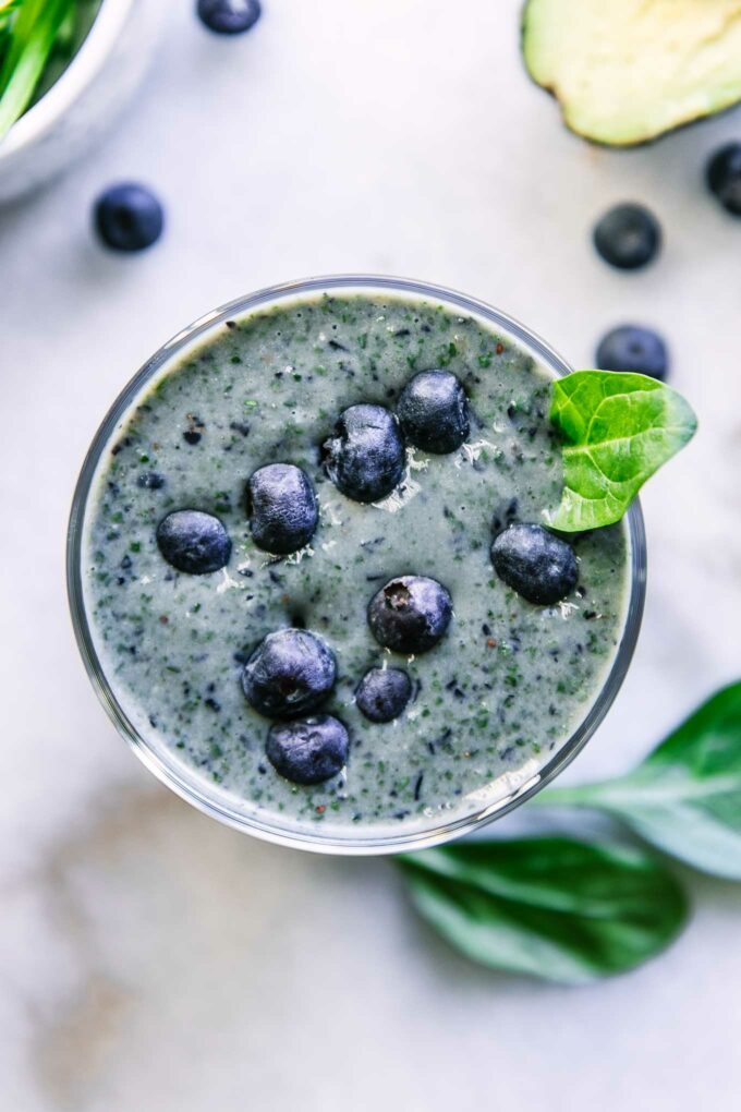 a close up photo of the top of a blueberry spinach smoothie garnished with a spinach leaf and fresh blueberries