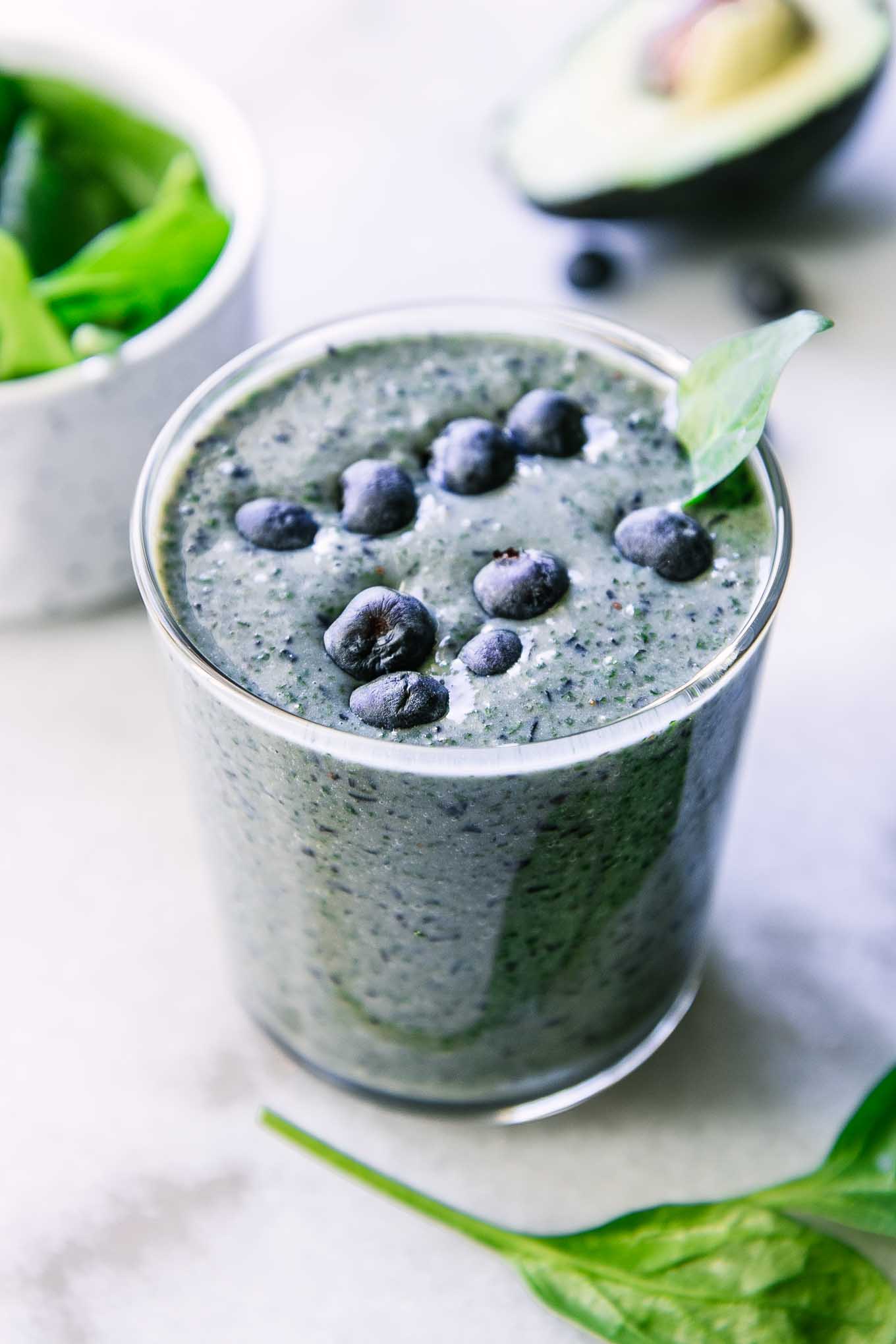 a spinach and blueberry smoothie in a glass on a white table