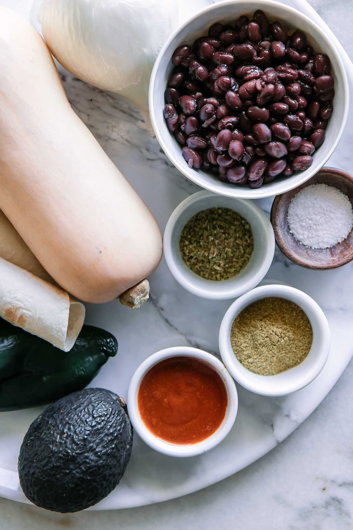 butternut squash, black beans, onion, avocados, and bowls of spices on a white table