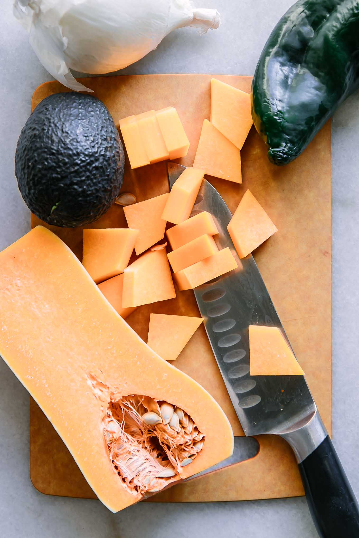 cut butternut squash on a cutting board with a poblano pepper