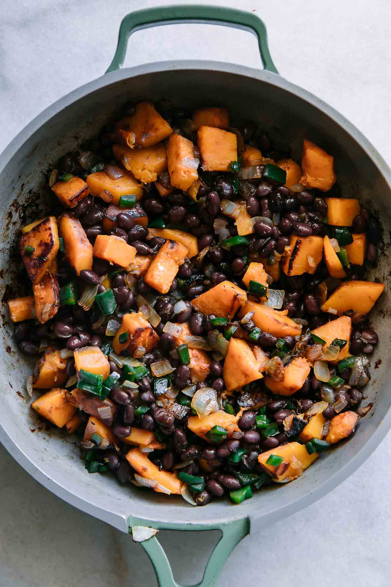 cooked butternut squash, black beans, onions, and spices for enchiladas in a green pan