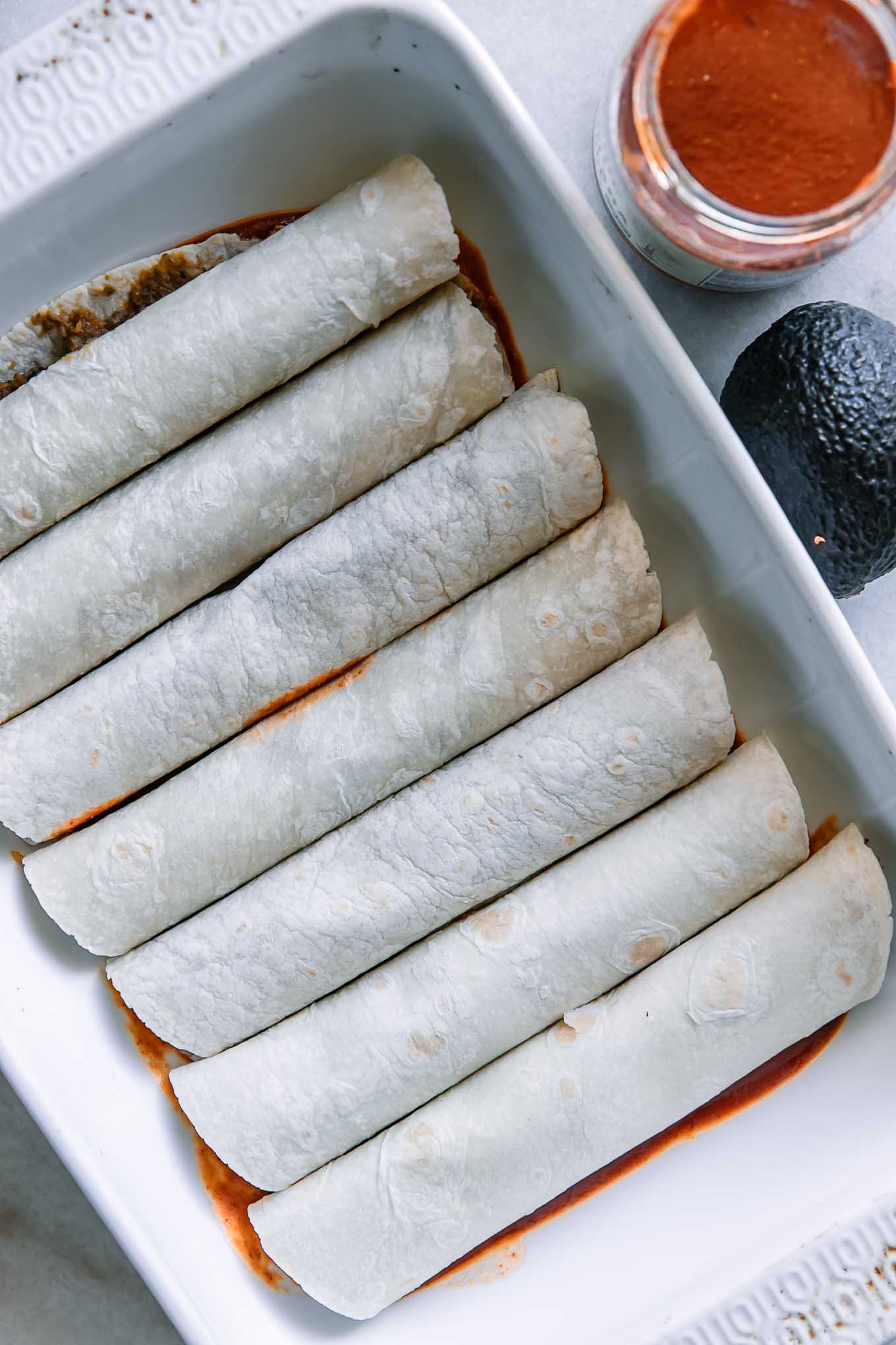 rolled enchiladas in a baking dish on top of red enchilada sauce