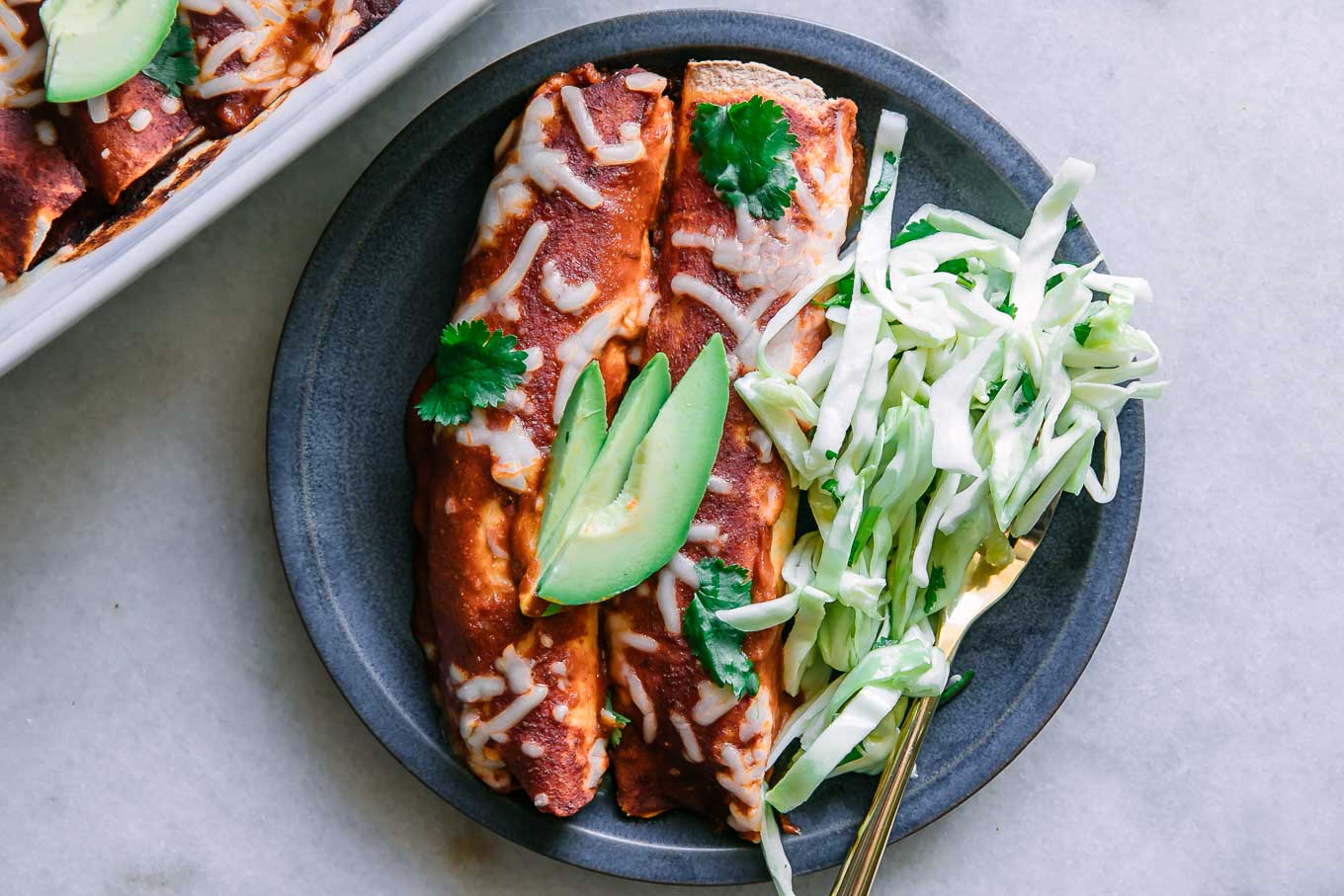 a blue plate with two butternut squash black bean enchiladas with avocado garnish on a white table