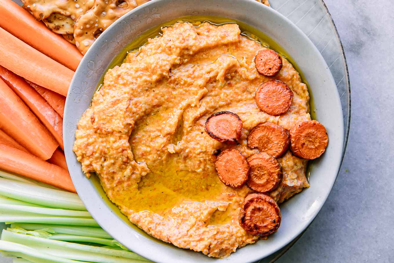 a bowl of carrot hummus dip on a plate with vegetables for dipping