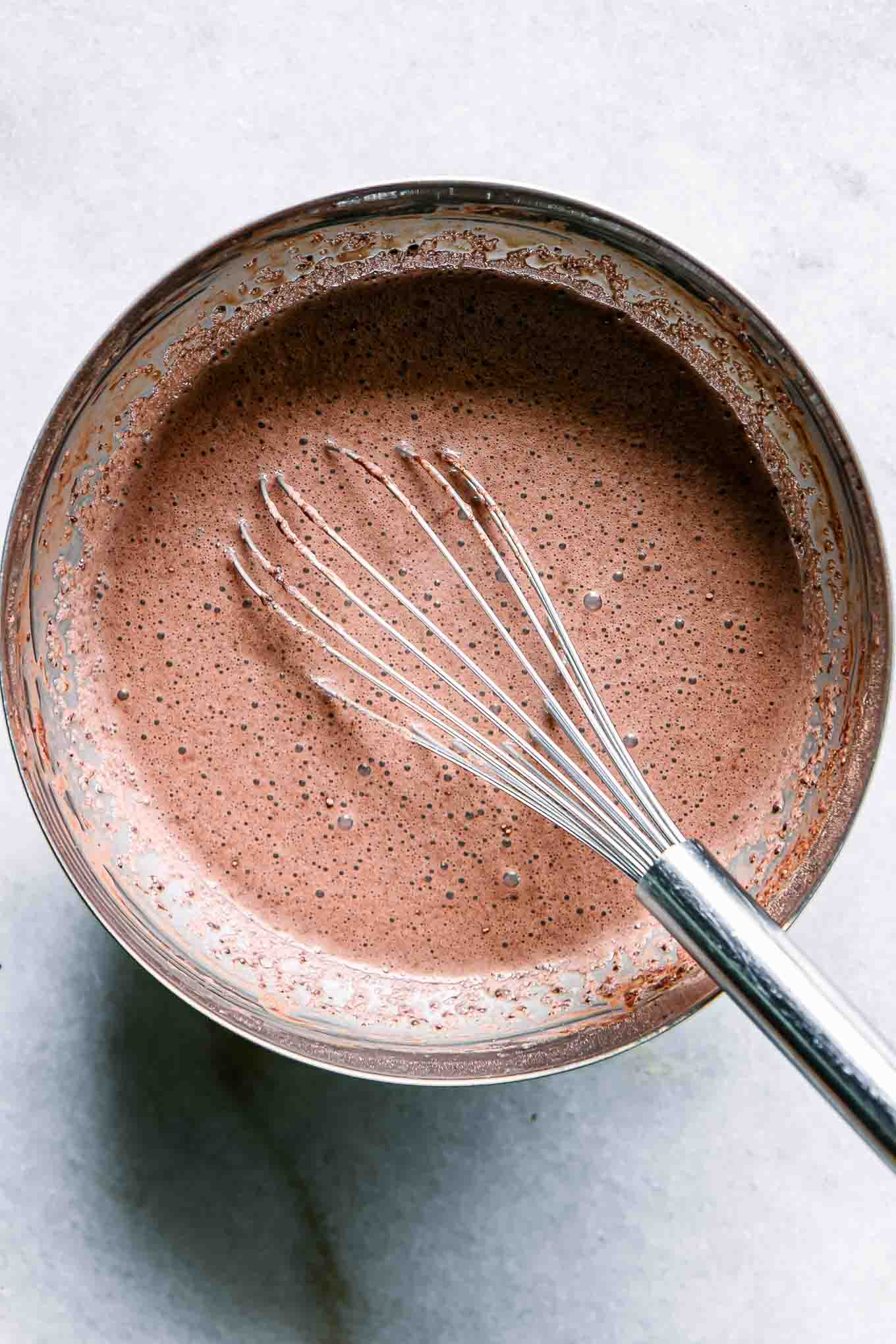a metal mixing bowl with chocolate chia seed pudding ingredients and a whisk