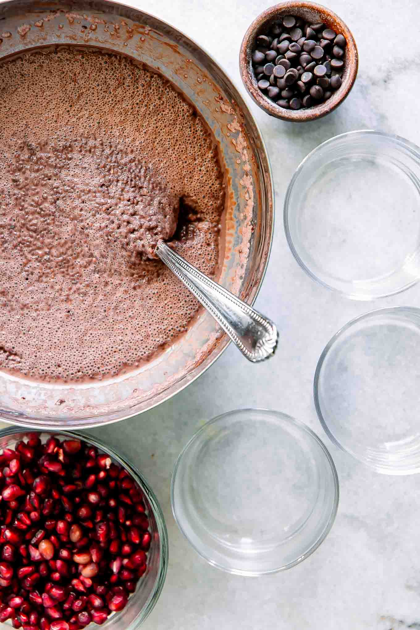 a bowl of chocolate chia pudding with small glass jars on a table