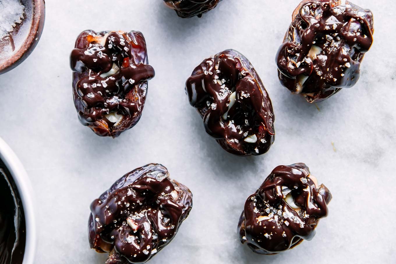 chocolate and peanut butter stuffed dates with flaky sea salt on a white table