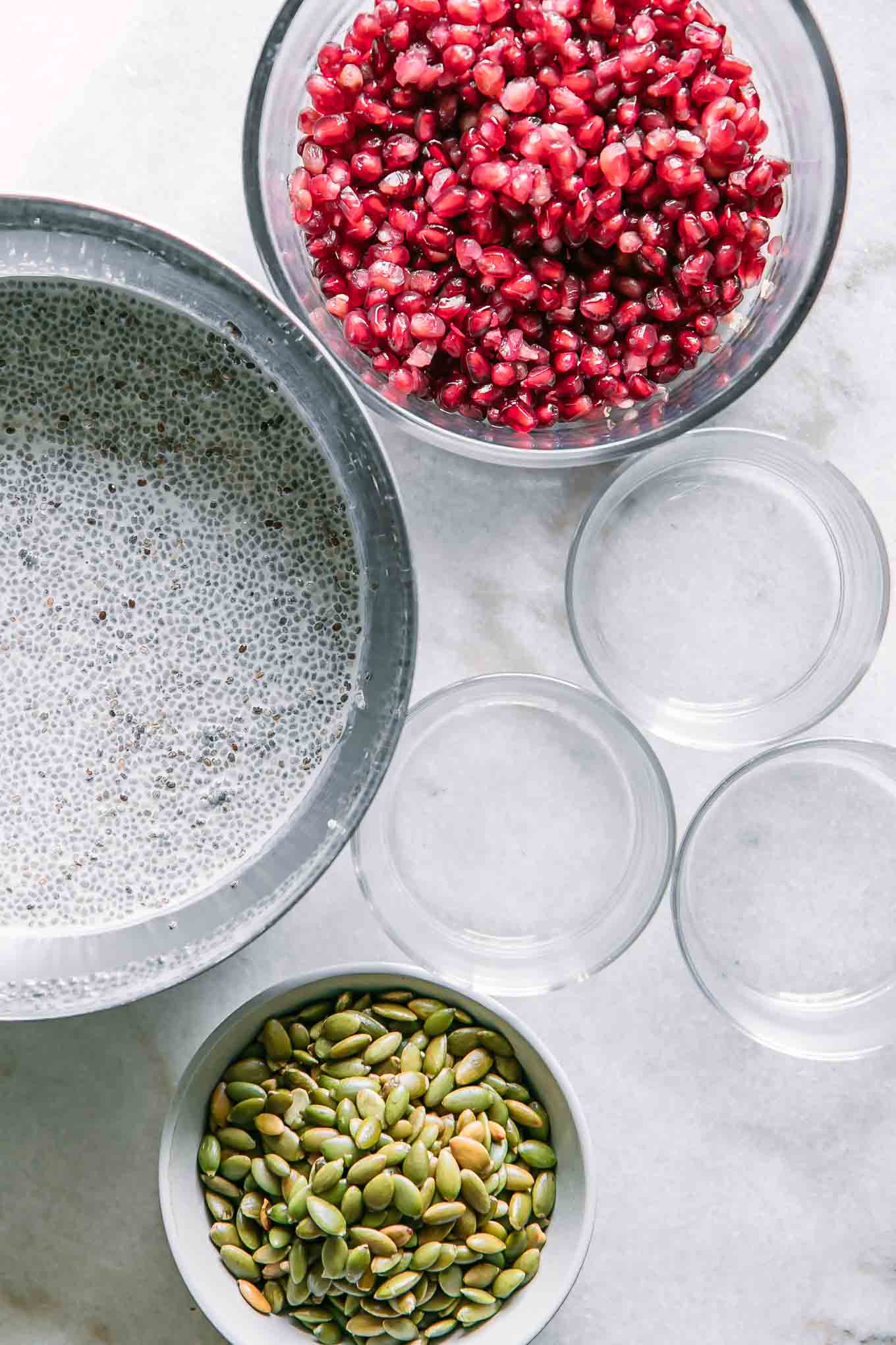 bowls of chia pudding, pomegranates, and seeds before building a chia seed pudding cup