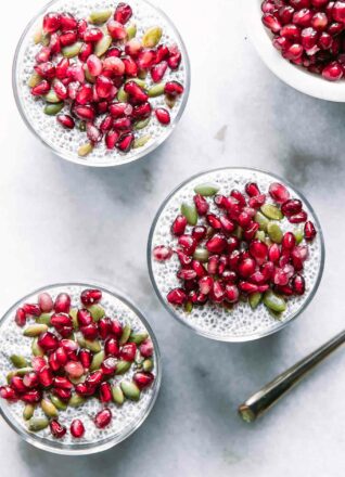 three jars of chia seed pudding with pomegranates and seeds on a white table