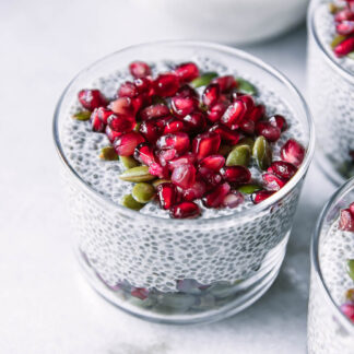 three small glass cups with pomegranate chia pudding and topped with seeds on a white table