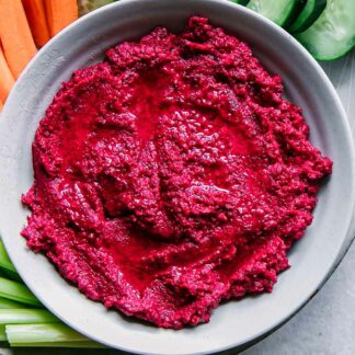 a bowl of red beet hummus on a plate with vegetable