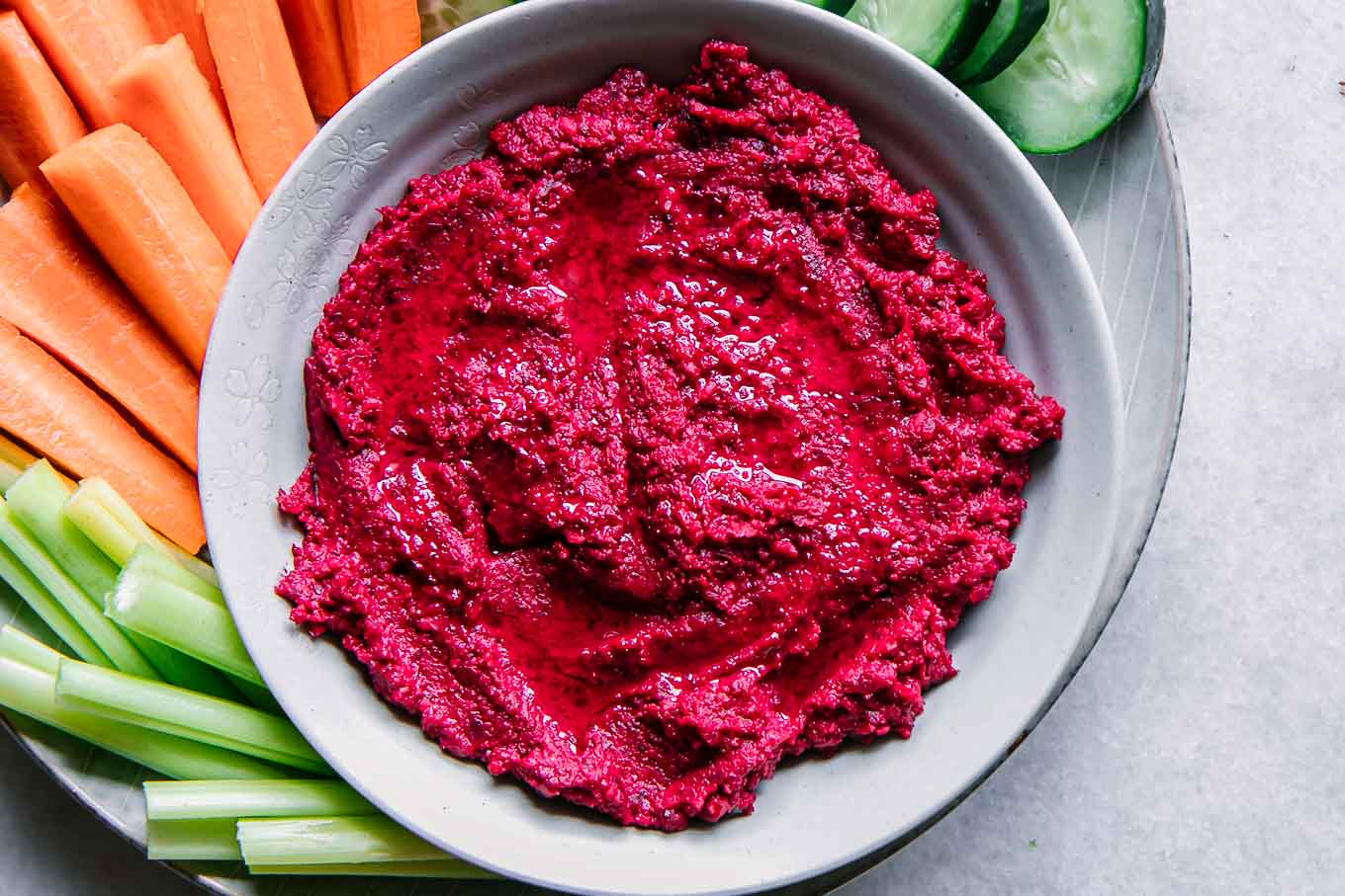 a bowl of red beet hummus on a plate with vegetable