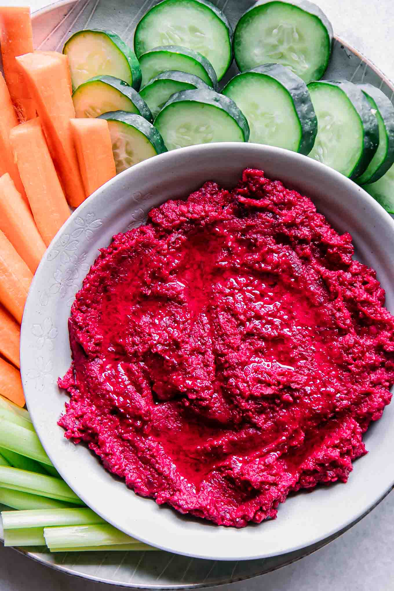 red beet hummus in a bowl with cut vegetables for dipping on a blue plate