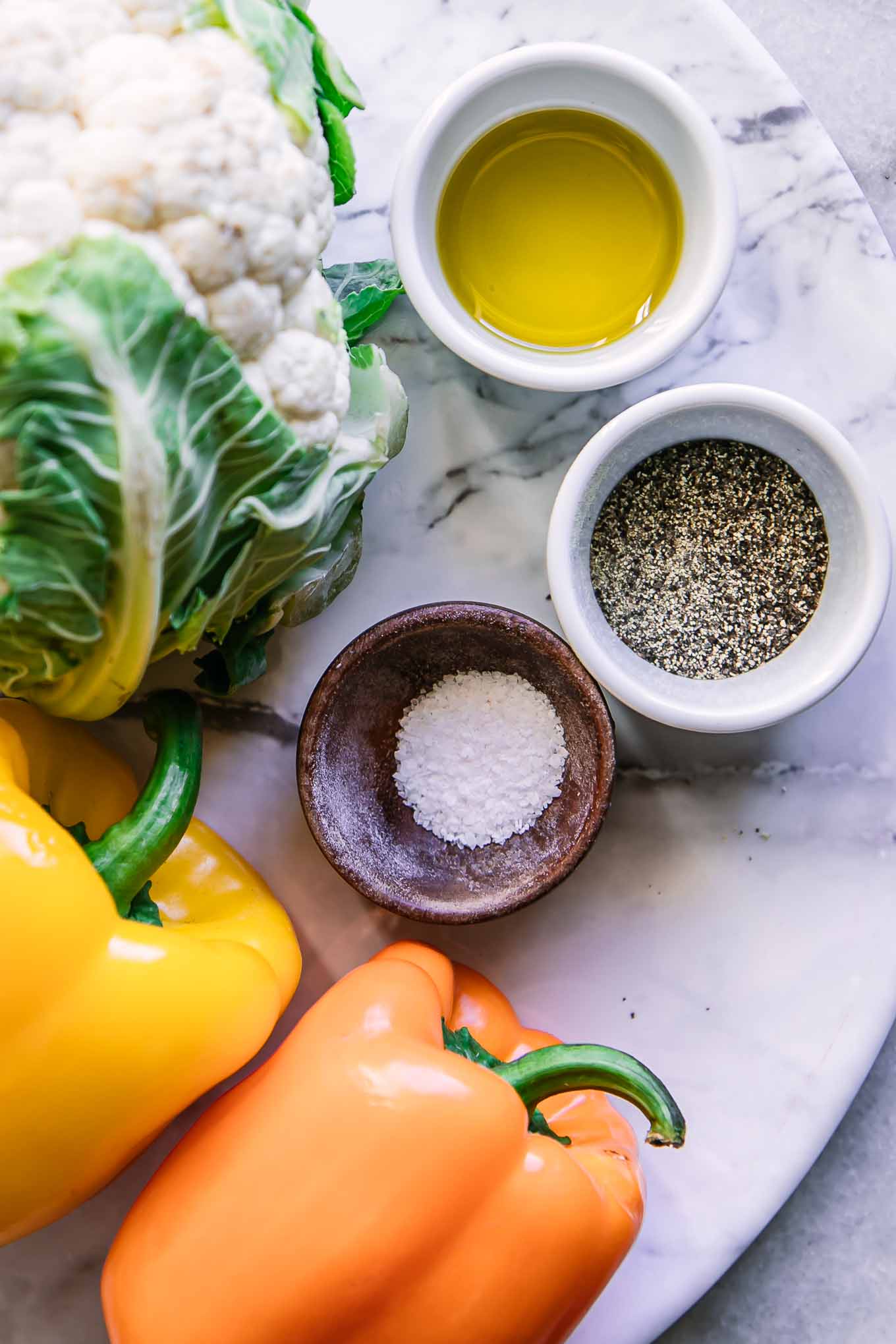 cauliflower, bell peppers, and bowls oil, salt, and pepper on a white table