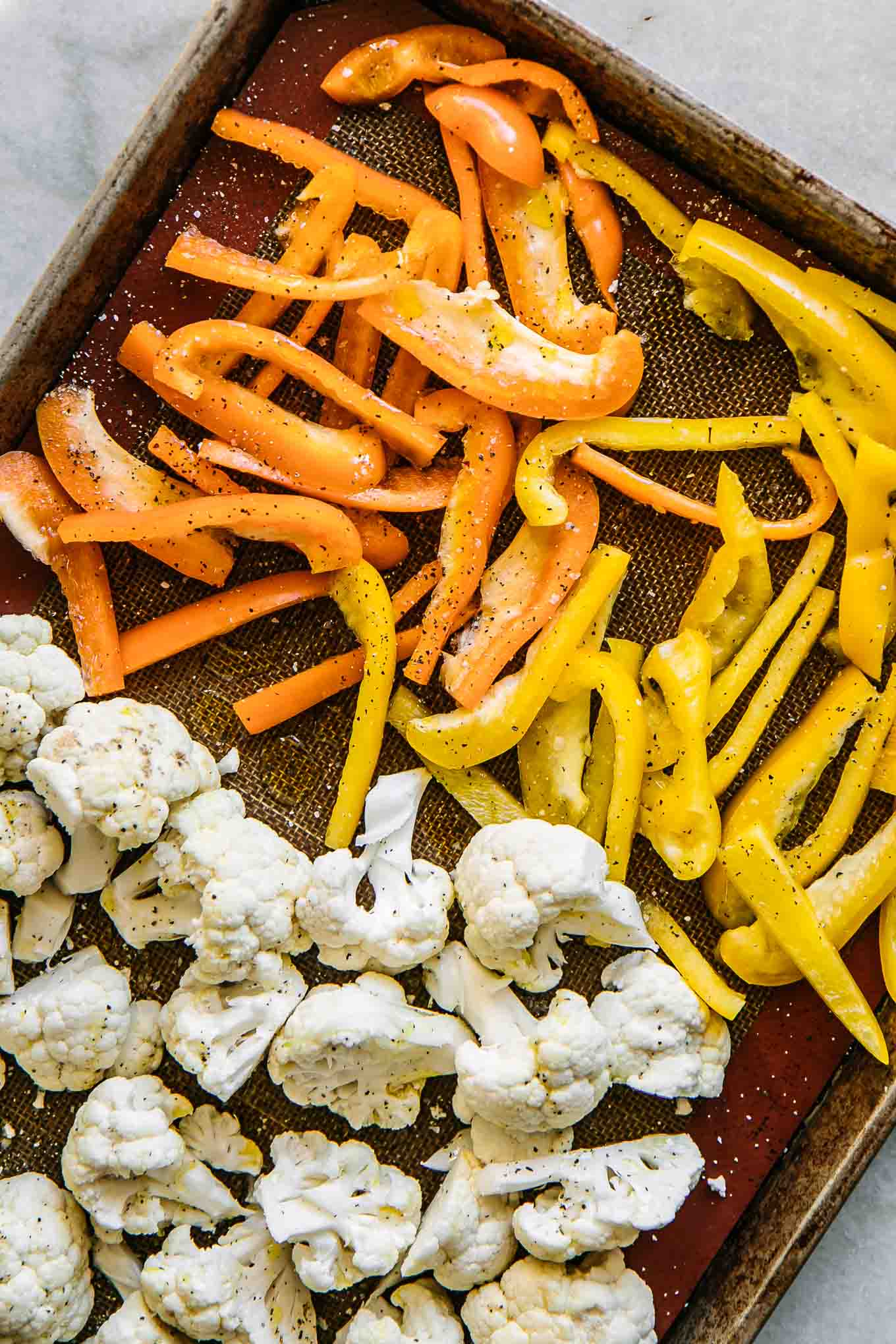 cut bell peppers and cauliflower on a baking sheet before roasting