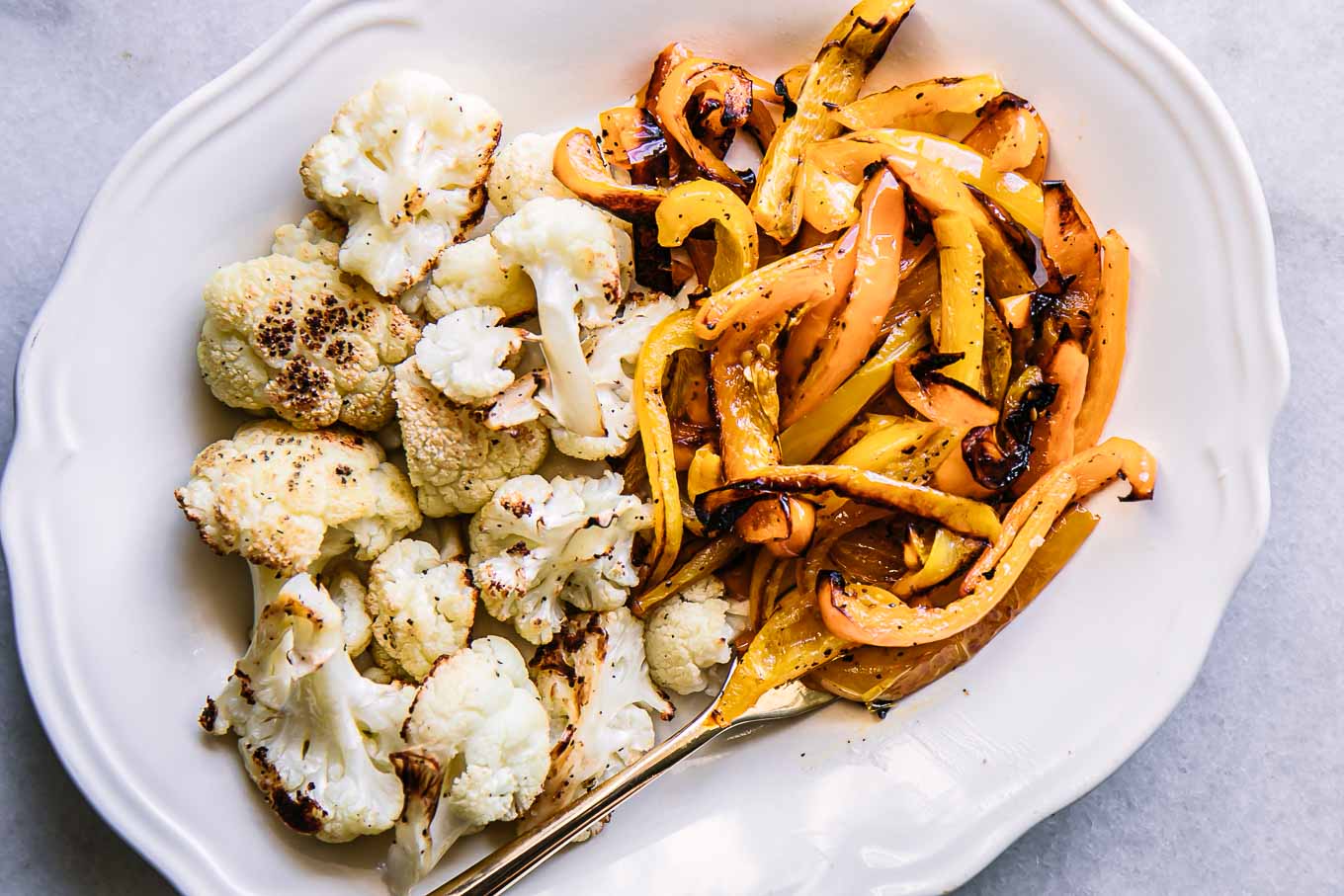 a white plate with roasted bell peppers and cauliflower with a gold fork on a white table