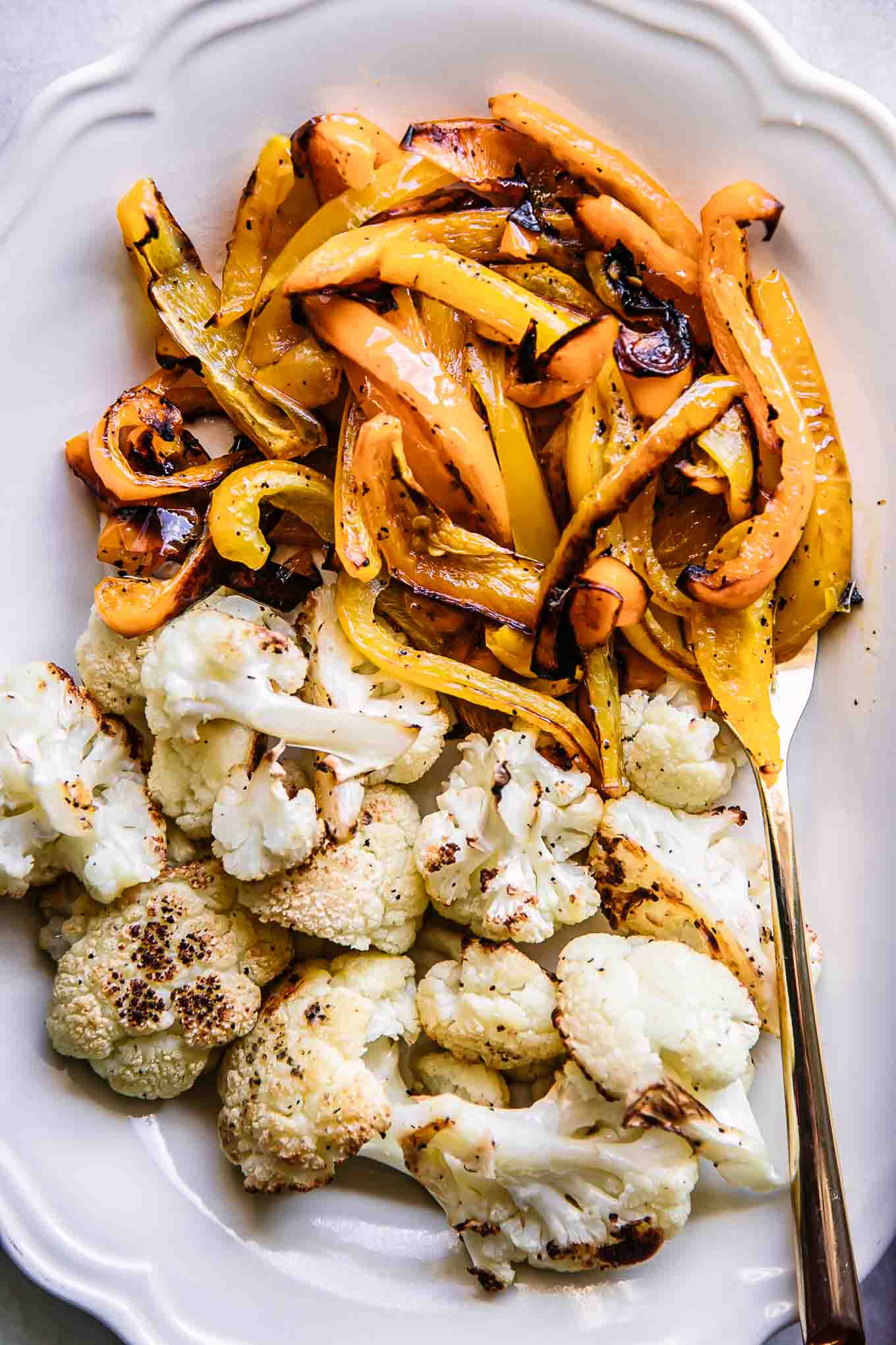 a closed up photo of baked bell peppers and cauliflower on a white plate