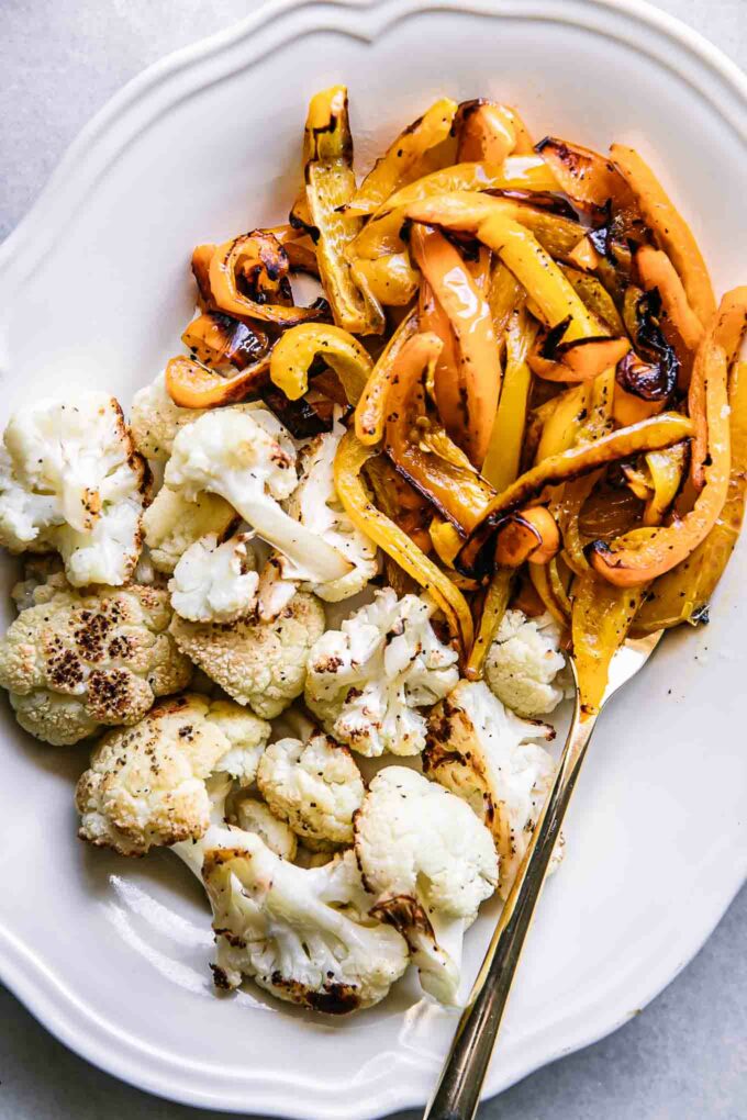 roasted cauliflower and bell peppers on a white plate with a gold fork
