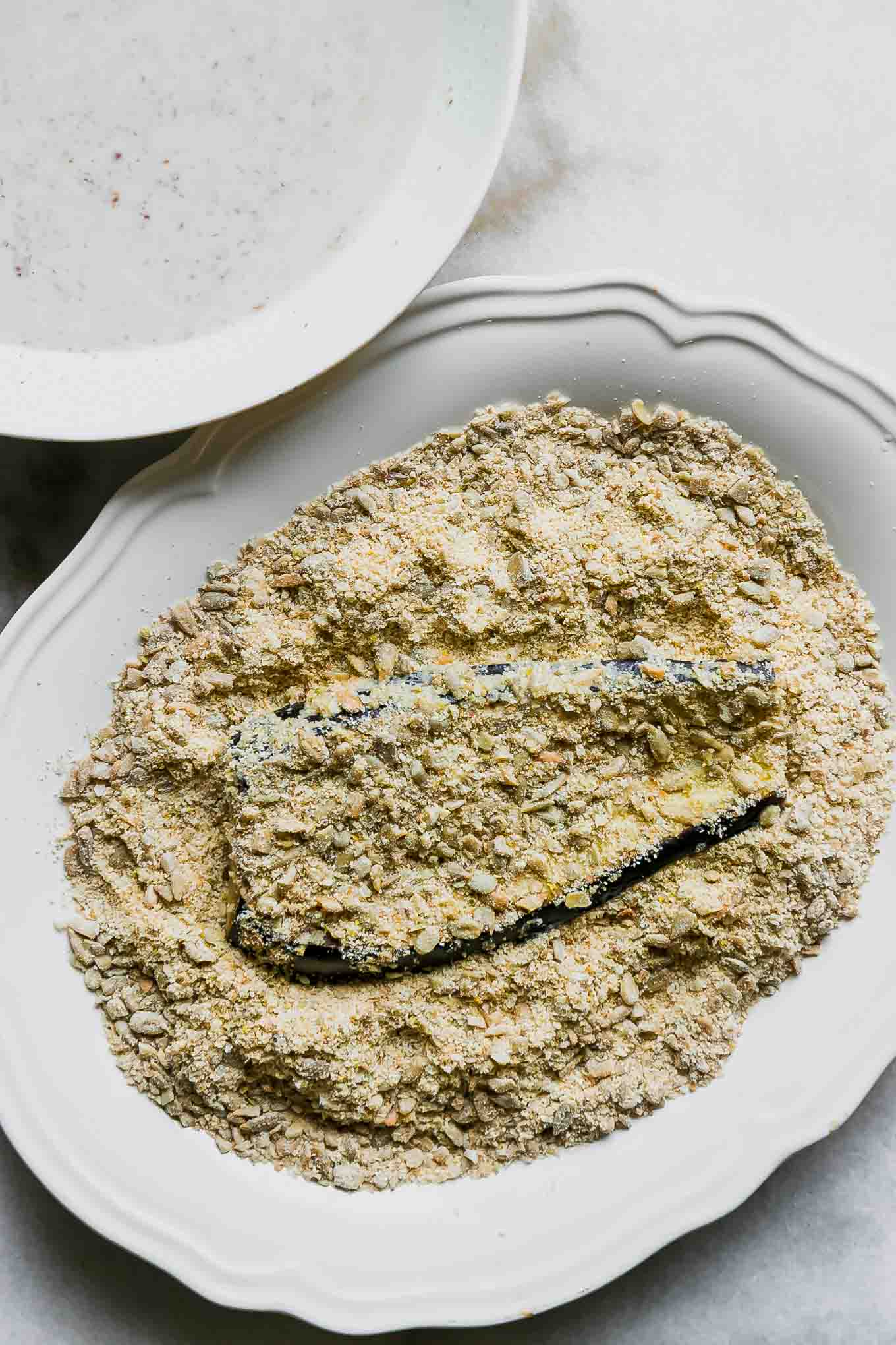 a piece of eggplant in a bread crumb mixture on a white plate