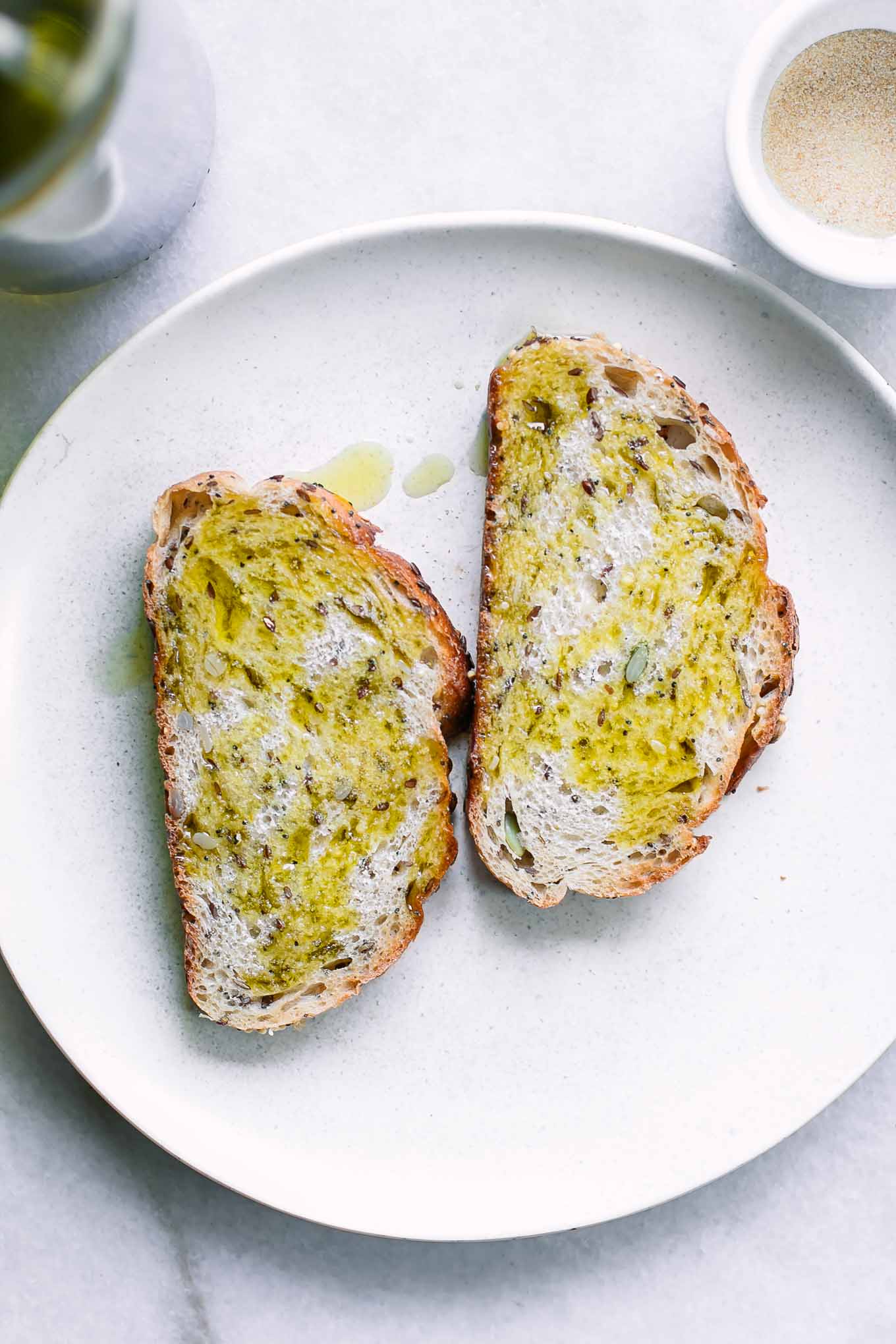 a white plate with two pieces of toast drizzled in olive oil and seasonings