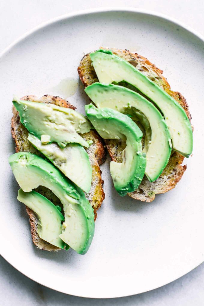 two pieces of bread with sliced avocado on a white plate