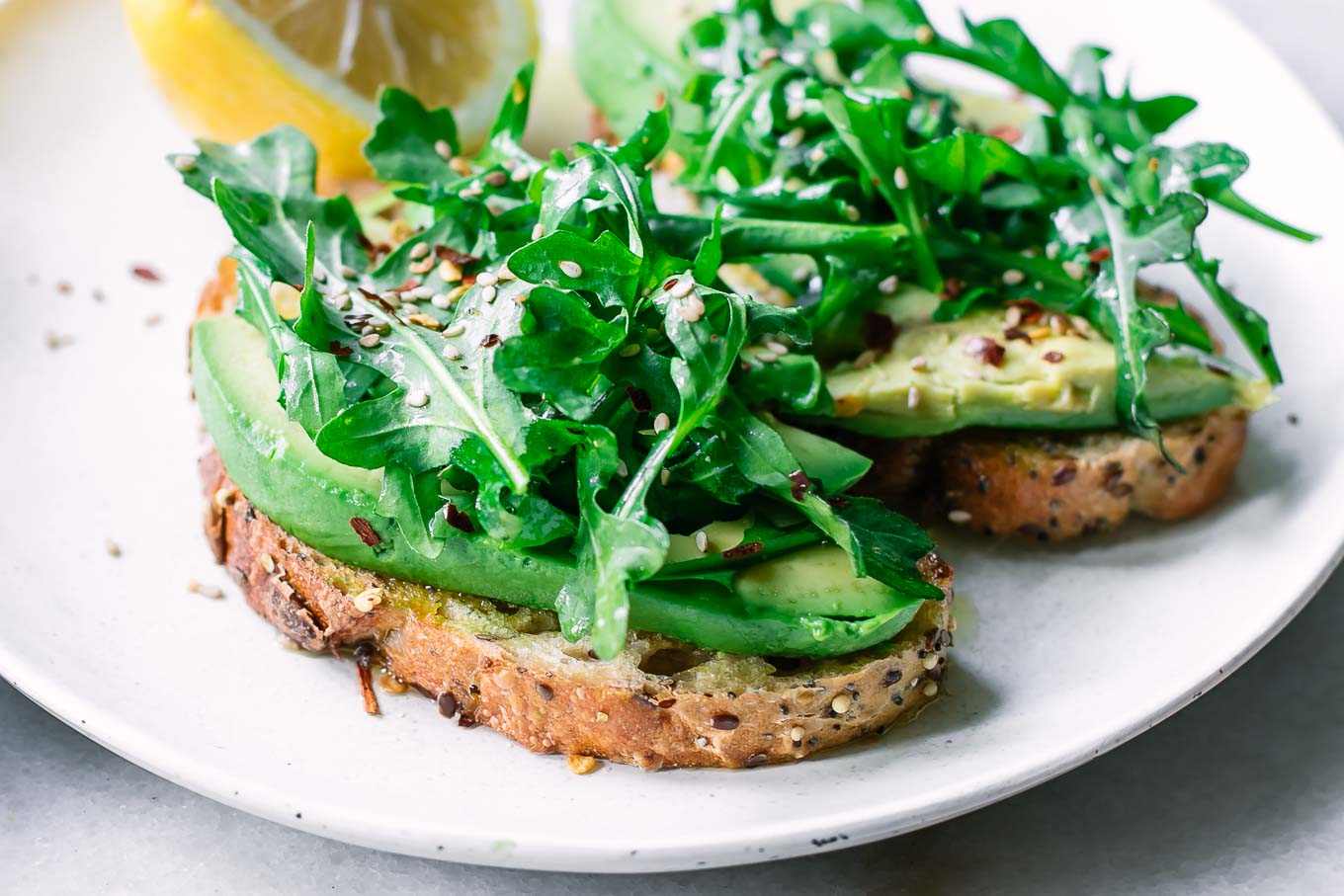 avocado toast with arugula on top on a white plate with a lemon