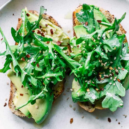 two pieces of lemon arugula avocado toast on a white plate