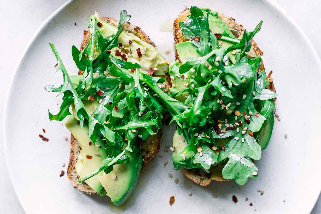 two pieces of lemon arugula avocado toast on a white plate