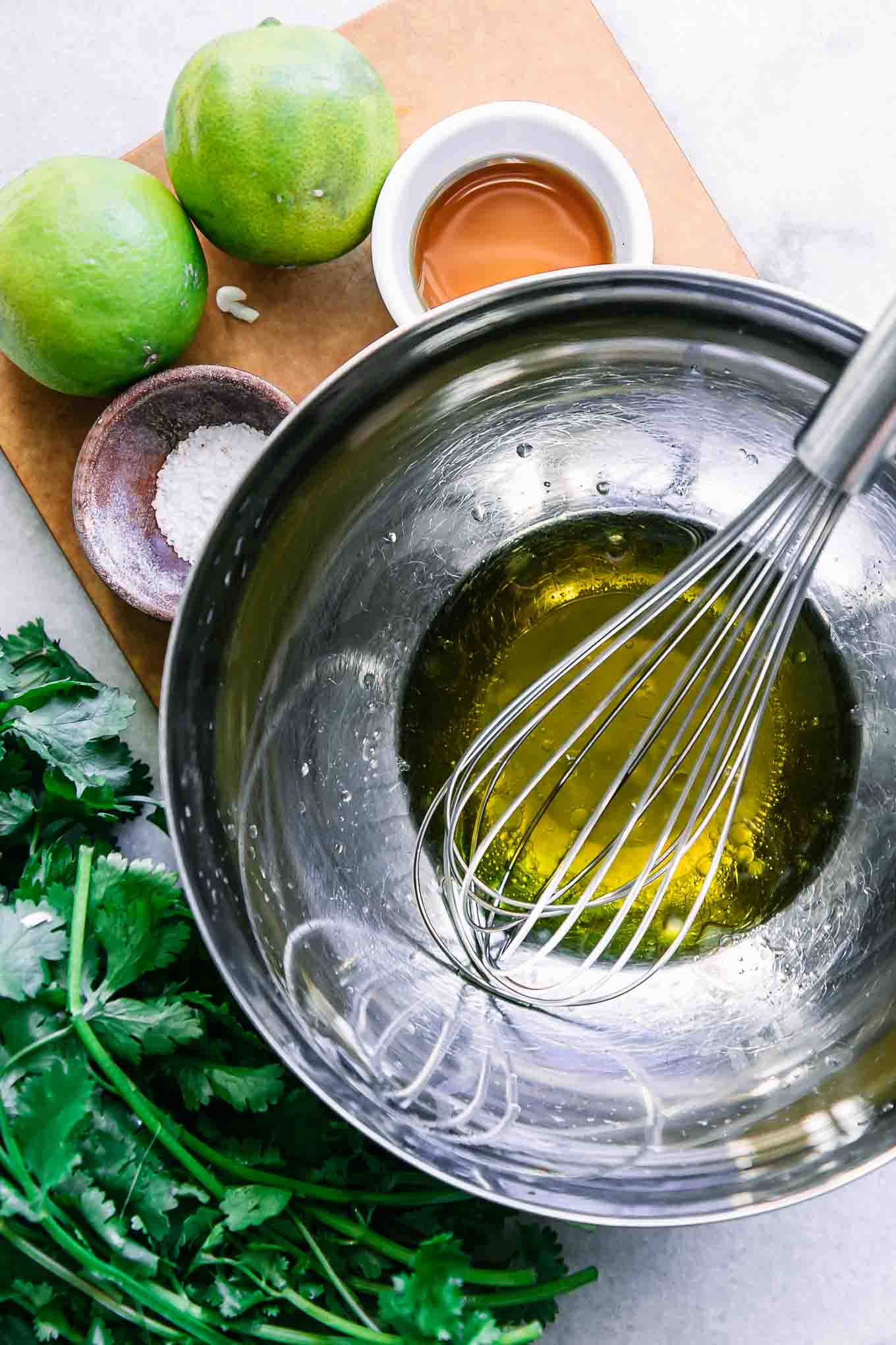 a metal mixing bowl with lime vinaigrette dressing ingredients on a white table