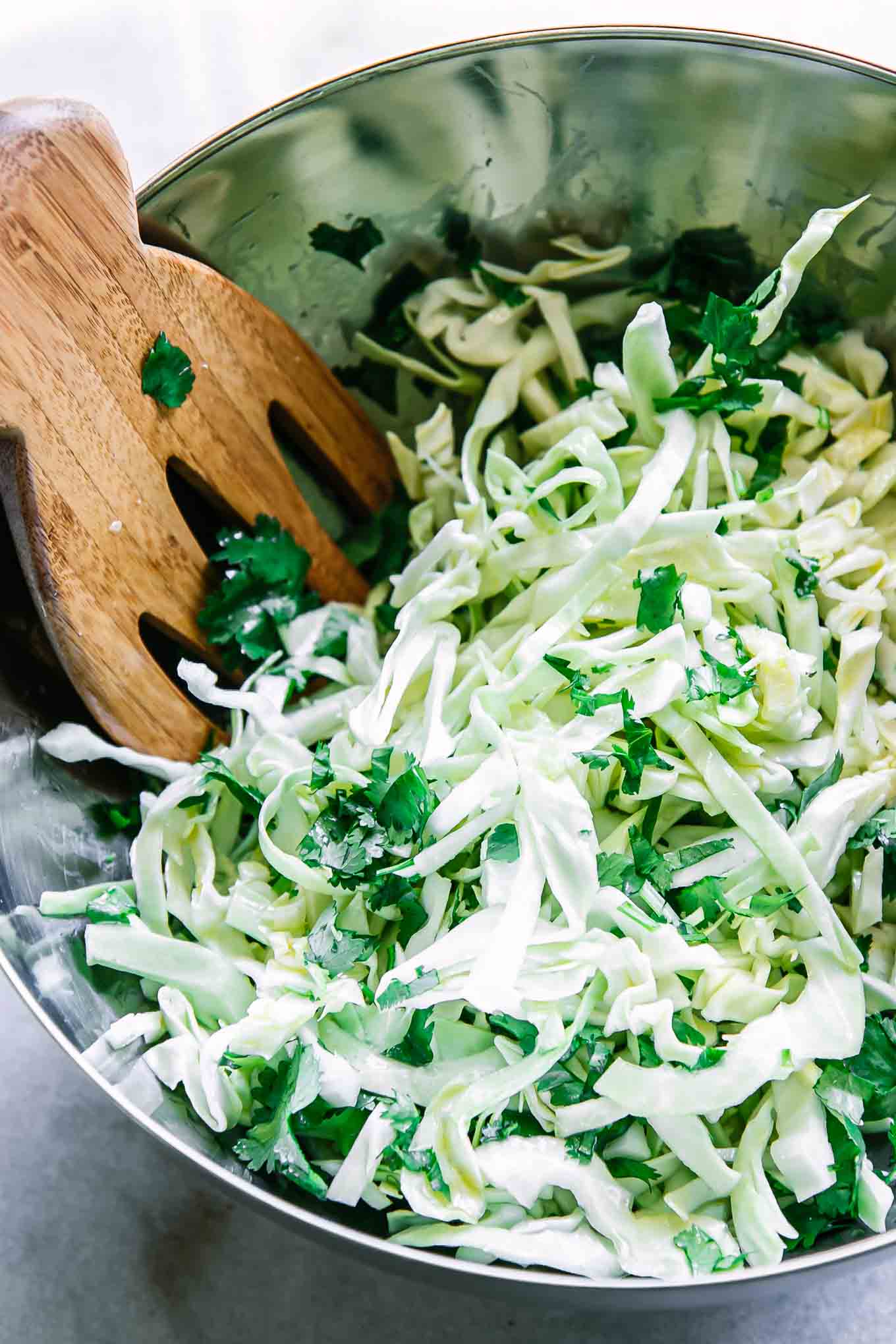 a close up photo of cabbage salad with chopped cilantro and lime dressing in a bowl