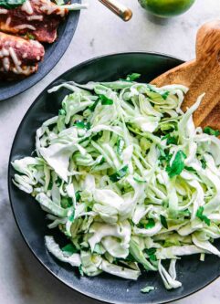 a sliced cabbage and cilantro slaw salad in a black bowl on a white table