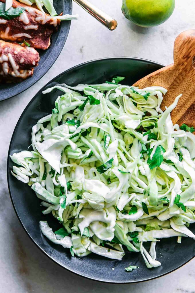 a sliced cabbage and cilantro slaw salad in a black bowl on a white table
