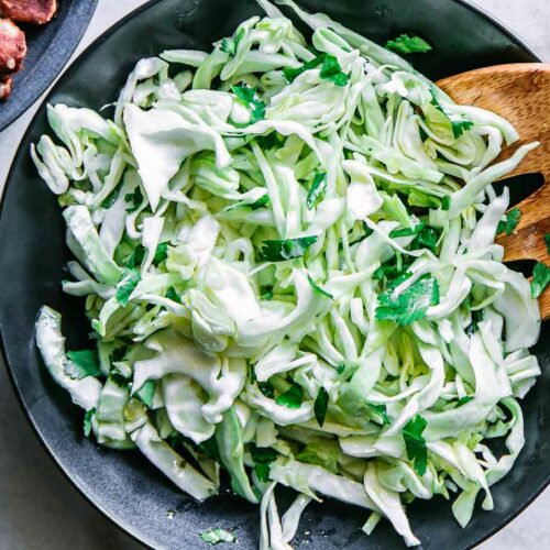 a cabbage cilantro and lime slaw salad in a black bowl on a white table with a lime