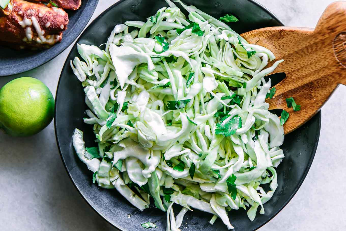 a cabbage cilantro and lime slaw salad in a black bowl on a white table with a lime