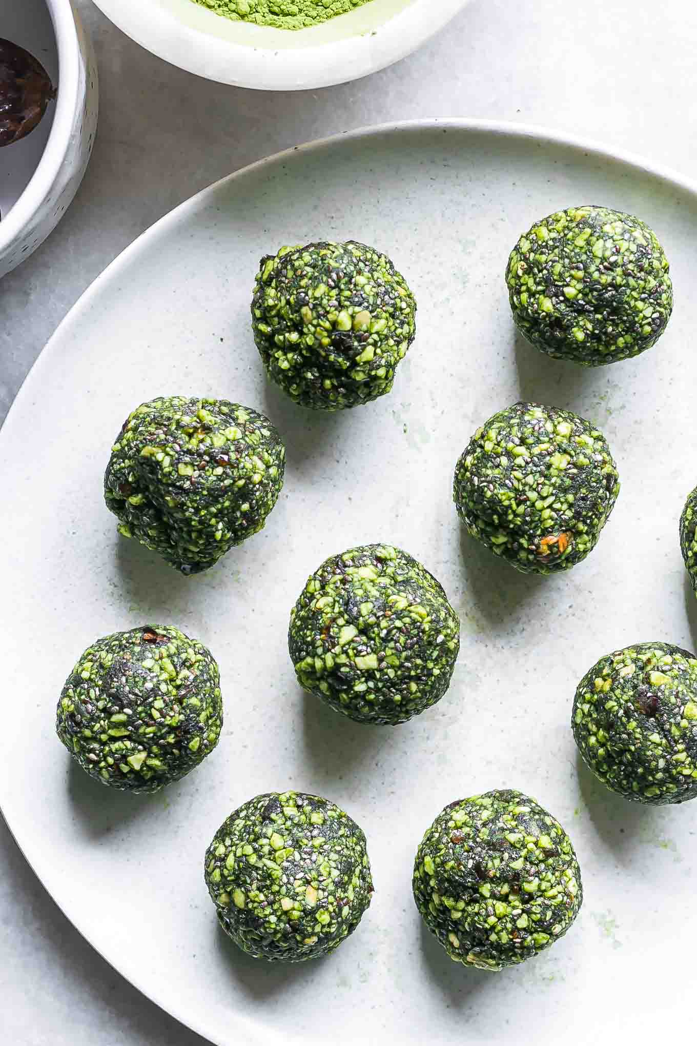 rolled green energy bites with matcha powder on a white table